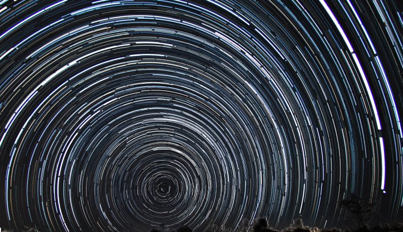 Une prise de vue à longue exposition capturant des étoiles qui s'étendent de façon circulaire dans le ciel nocturne pendant la rotation de la terre.