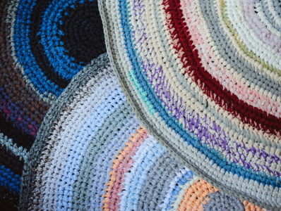 A pile of colourful rugs, each consisting of textiles that have been upcycled and woven together.