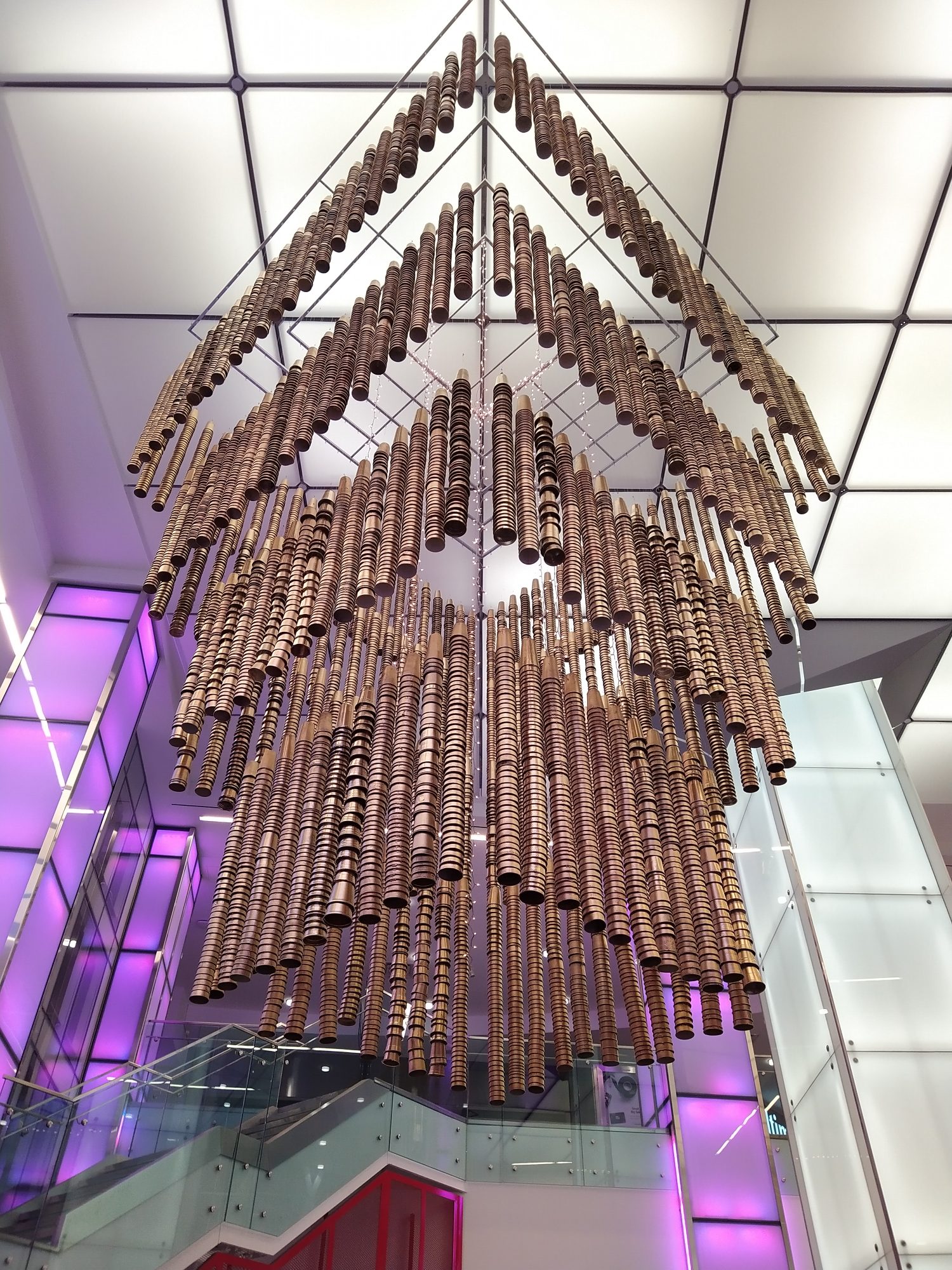 The Awakening, a huge waste-based sculpture, hangs from the ceiling in a mall's atrium. Resembling a chandelier, the "crystals" are made with discarded single-use cups made to look bronze.
