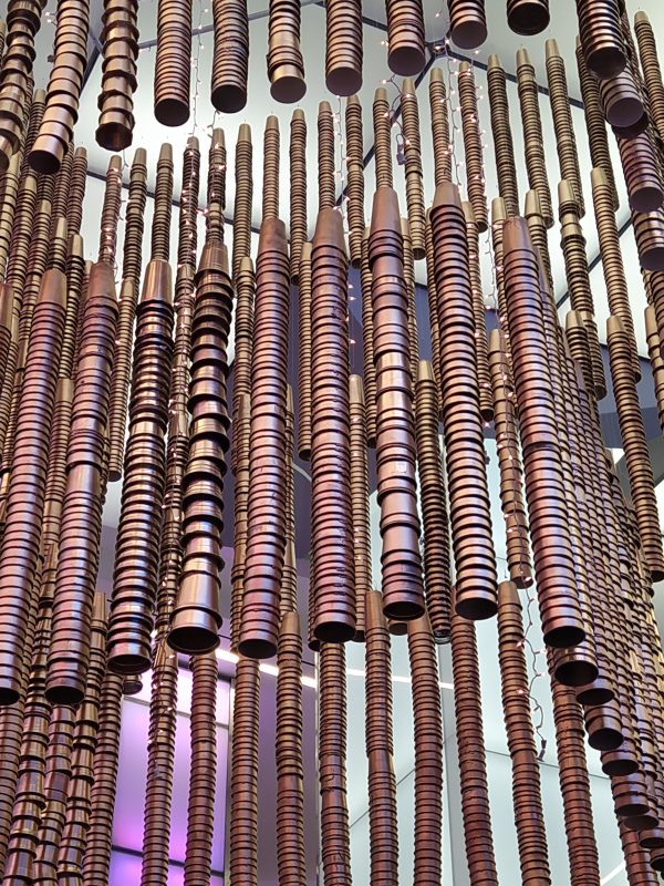 A close-up look at the materials used in the sculptural installation, The Awakening. Bronze-coated, stacked single-use cups hang in tiers within a chandelier-like frame.