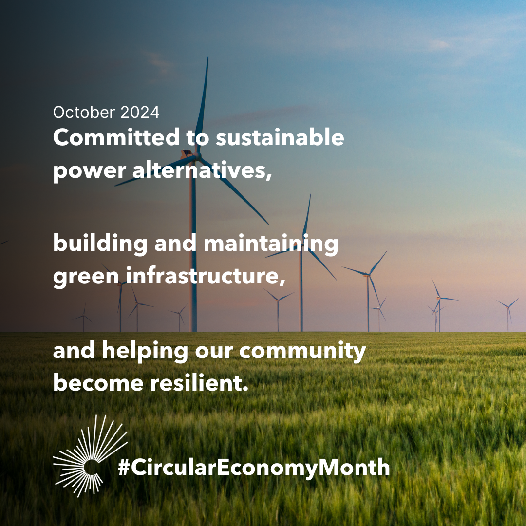 A flat field featuring a wind turbine farm extends into the distance, with a beautiful sunrise sky along the horizon. October 2024. Committed to sustainable power alternatives. Building and maintaining green infrastructure. Helping our community become resilient. #CircularEconomyMonth